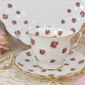 May include: A white teacup and saucer with a delicate pink rose pattern. The cup and saucer have a gold trim around the edges.