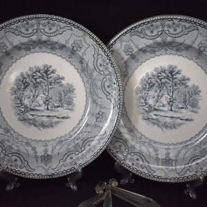 May include: Two vintage blue and white porcelain plates with a decorative border and a central image of a cottage in a wooded landscape.