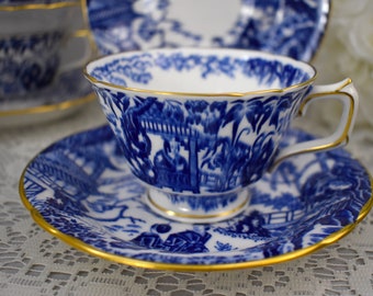 May include: A blue and white teacup and saucer with a gold trim. The teacup and saucer feature a traditional Chinese design with a landscape scene.