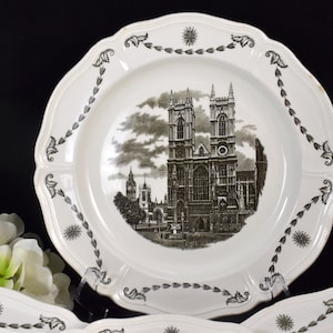 May include: White ceramic plate with a black and white image of Westminster Abbey in London. The plate has a decorative border with a repeating leaf design.