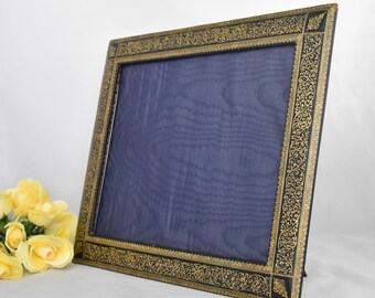 May include: A black picture frame with a gold ornate design. The frame has a blue velvet backing.