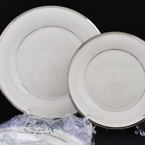 May include: Two white ceramic dinner plates with silver trim. The larger plate is behind the smaller plate.