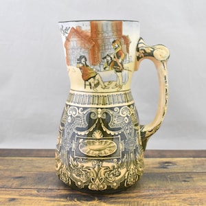 May include: A vintage ceramic beer stein with a detailed handle and a decorative design. The stein features a scene of people in a town setting, with intricate patterns in black, beige, and brown. The stein is on a wooden surface.