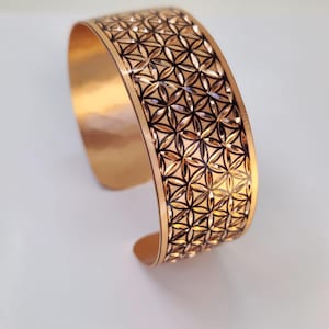 Può includere: Un braccialetto in rame con un motivo geometrico a forma di fiore della vita. Il braccialetto è di colore rame caldo con un design nero.