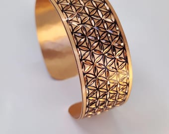Può includere: Un braccialetto in rame con un motivo geometrico a forma di fiore della vita. Il braccialetto è di colore rame caldo con un design nero.