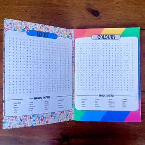 May include: A colorful word search puzzle book with two pages. The left page has a food theme and the right page has a colors theme. The words to find are listed below each puzzle.