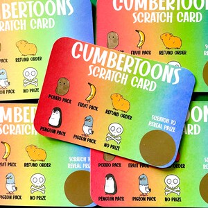 Puede incluir: Una tarjeta de rascar colorida con el texto "Cumbertoons Scratch Card" e im&aacute;genes de un ping&uuml;ino, una paloma, una patata, un pl&aacute;tano, un conejillo de indias y una calavera. La tarjeta tiene un &aacute;rea de rascar plateada para revelar un premio.