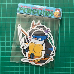 Puede incluir: Un conjunto de cuatro pegatinas de Teenage Mutant Ninja Penguin. Las pegatinas muestran a los ping&uuml;inos vestidos como las Tortugas Ninja, cada uno con sus colores y armas caracter&iacute;sticos. Las pegatinas est&aacute;n empaquetadas en una bolsa de pl&aacute;stico transparente con un encabezado que dice "Cumbertoons Teenage Mutant Ninja Penguins".