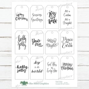 Könnte beinhalten: Ein Bogen weißer Geschenkanhänger mit schwarzer Kalligraphie. Auf den Anhängern stehen festliche Sätze wie „Fröhliche Weihnachten“, „Frieden auf Erden“ und „Freude für die Welt“. Die Anhänger sind rechteckig mit einem Loch oben.
