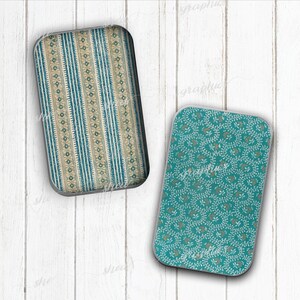 May include: Two rectangular decorative trays. One features a blue and beige striped pattern with floral accents. The other has a teal background with a white and beige floral design. Both have rounded corners and a silver trim.