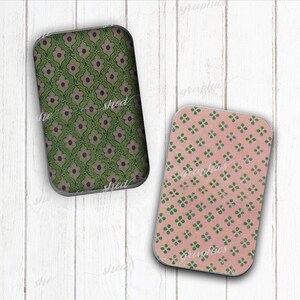 May include: Two rectangular coasters with rounded corners. One has a green floral pattern with pink accents, the other a pink background with green and yellow floral designs. The coasters are on a white wooden surface.