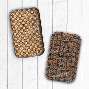 May include: Two rectangular decorative trays. One features a repeating pattern of yellow circles with red and brown accents. The other has a dark blue background with orange and brown leaf designs. Both have a silver trim.