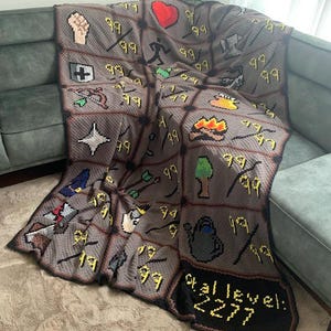 Puede incluir: Una manta de ganchillo gris hecha a mano con varios iconos de juego pixelados y el texto "Total level: 2277" en amarillo. La manta presenta un dise&ntilde;o de cuadr&iacute;cula con iconos como un pu&ntilde;o, un coraz&oacute;n y flechas.