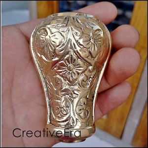 Puede incluir: Un mango de bastón de metal dorado con un intrincado diseño floral.