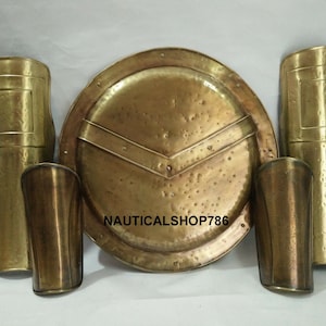May include: A set of three gold-colored metal armor pieces, including a round shield with a V-shaped design, and two arm guards. The shield has the text "NAUTICALS SHOP786" on it.