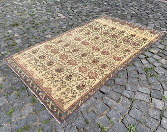 May include: A vintage cream-colored rug with a floral pattern in shades of red, brown, and green. The rug has a border with a geometric design.