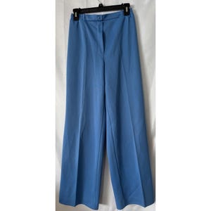 May include: Light blue wide-leg pants. The pants have a button and zipper closure at the waist and are hanging on a black hanger. The fabric appears to be a smooth, solid color. The pants are a classic style.