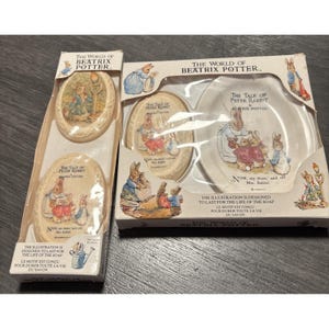 Könnte beinhalten: Zwei Sets mit Seifenschalen und Seife zum Thema Beatrix Potter. Die Sets zeigen Illustrationen aus "The Tale of Peter Rabbit". Der Text auf den Schachteln lautet "The World of Beatrix Potter" und "Die Illustration ist für die Lebensdauer der Seife bestimmt."