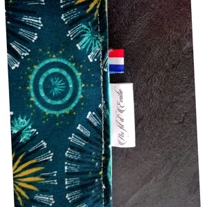 May include: A green fabric with a yellow and white pattern. The fabric has a label that says "Au Fil d'Emilie" with a small French flag.