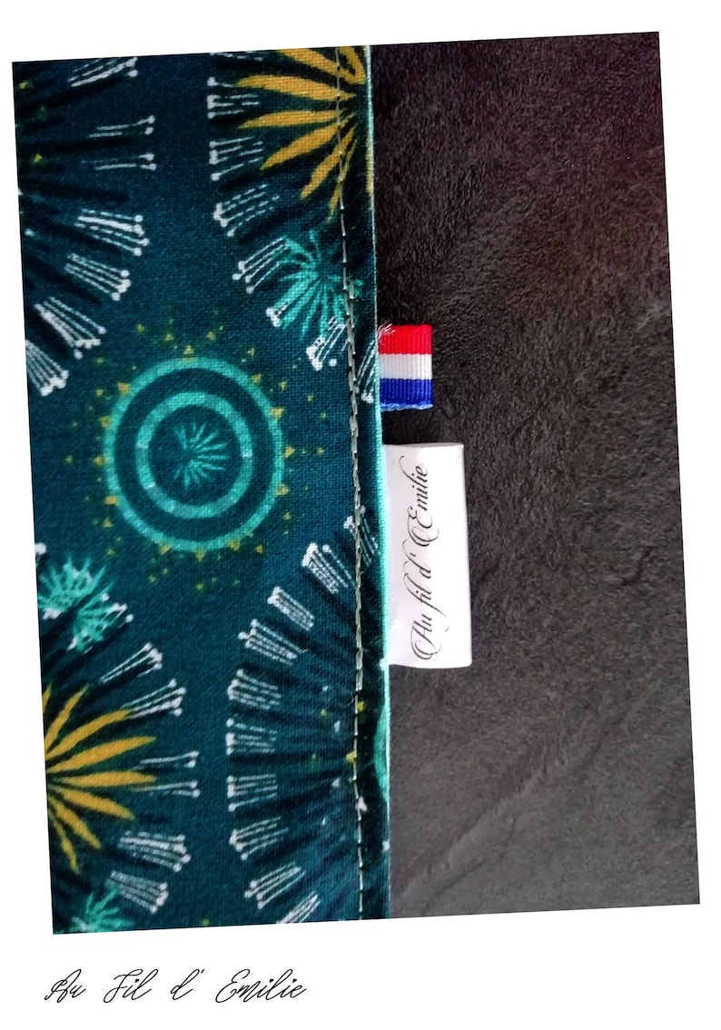 May include: A green fabric with a yellow and white pattern. The fabric has a label that says "Au Fil d'Emilie" with a small French flag.