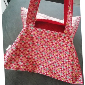 May include: Red and white tote bag with a geometric pattern of green, yellow, and red ovals. The bag has red handles and a red lining. The bag is made of fabric and has a label that says "Au Fil d'Emilie".