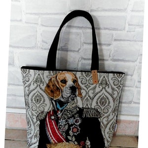 Può includere: Una borsa tote nera con un tessuto beige che presenta un beagle che indossa un'uniforme militare. Il tessuto ha un motivo damascato. La borsa ha manici neri e un piccolo cartellino marrone con il testo "Au Fil d'Emilie".