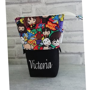 Peut inclure: Une pochette noire zippée avec une doublure en tissu sur le thème d'Harry Potter. La pochette a un tirette de fermeture éclair blanche et le nom "Victoria" est brodé sur le devant en fil blanc.