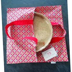 May include: A red and white fabric tote bag with a red handle. The bag is lined with a cream-colored fabric and has a red and white geometric pattern. The bag is filled with a ceramic plate. The bag has a tag that says "Handmade with Love" and a business card that says "Au Fil d'Emilie".