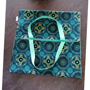 May include: A green tote bag with a geometric pattern of circles and yellow accents. The bag has two light green straps.