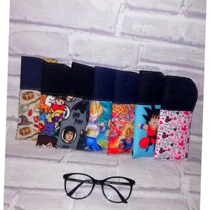 Peut inclure: Six étuis à lunettes colorés avec différents personnages de dessins animés, dont Harry Potter, Dragon Ball Z et Mickey Mouse. Les étuis sont doublés de tissu noir et ont un rabat en jean. Une paire de lunettes noires est au premier plan.