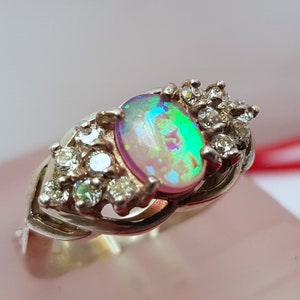 May include: A silver ring with a large oval opal gemstone surrounded by smaller clear gemstones. The ring is set on a white background.