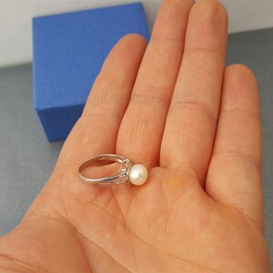 May include: A silver ring with a white pearl set in a silver band. The ring is on a hand.