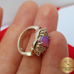 May include: A silver ring with a pink opal gemstone surrounded by smaller clear gemstones. The ring is set in a delicate, intricate design.