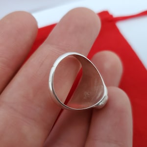 Może przedstawiać: Srebrny pierścionek z gładką, zaokrągloną obręczą. Wewnętrzna strona obręczy jest widoczna, pokazując małe oznaczenie.