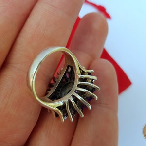 May include: A silver ring with a large purple gemstone surrounded by smaller purple gemstones. The ring is set in a silver band with a delicate design.