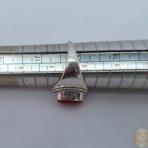 Może przedstawiać: Srebrny pierścionek z czerwonym kamieniem szlachetnym osadzonym w oprawie typu bezel. Pierścionek jest dopasowany do rozmiaru na mierniku pierścionk&oacute;w, pokazując rozmiar 8.