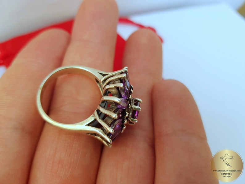 May include: A silver ring with a cluster of purple amethyst stones set in a delicate, intricate design.