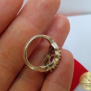 May include: A silver ring with a floral design and purple gemstones. The ring is on a finger.
