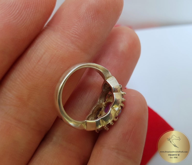 May include: A silver ring with a floral design and purple gemstones. The ring is on a finger.