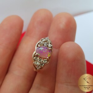 May include: A silver ring with a pink opal gemstone surrounded by smaller clear gemstones.