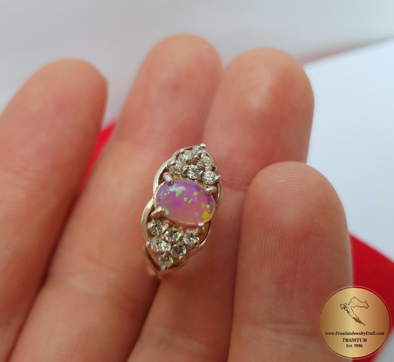 May include: A silver ring with a pink opal gemstone surrounded by smaller clear gemstones.