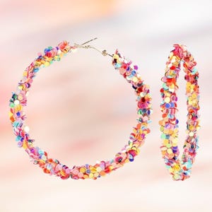 May include: A pair of hoop earrings covered in colorful sequins. The earrings feature a variety of colors, including pink, yellow, orange, and blue. The hoops are connected with a silver clasp.