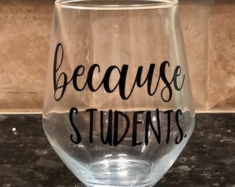 May include: A clear stemless wine glass with the words "because STUDENTS." in black script. The glass is sitting on a dark countertop.