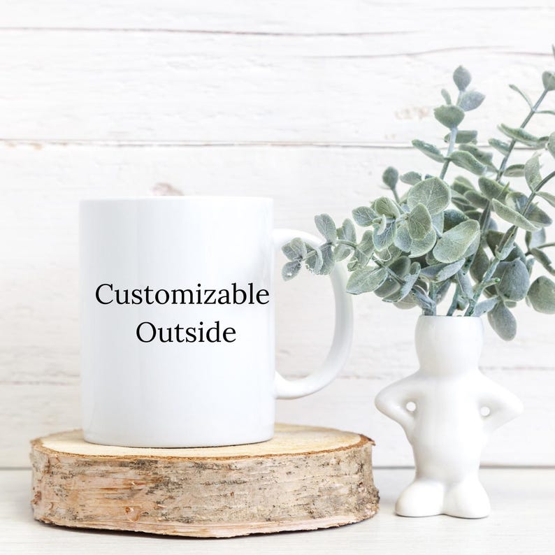 Peut inclure: Une tasse en c&eacute;ramique blanche avec une inscription noire qui dit "Customizable Outside". La tasse est pos&eacute;e sur un sous-verre en bois et il y a un petit vase en c&eacute;ramique blanche avec une plante verte en arri&egrave;re-plan.