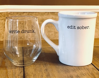 May include: A white ceramic mug with the text "edit sober." next to a clear glass with the text "write drunk."