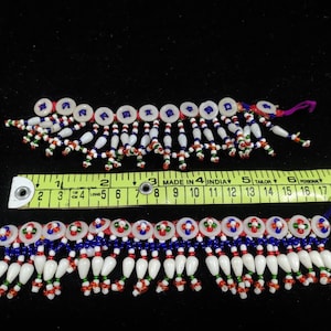 Può includere: Due pezzi di bordura con perline bianche, blu, rosse e verdi. I pezzi di bordura hanno una frangia di perline bianche e una fila di bottoni rotondi bianchi con accenti blu e rossi.