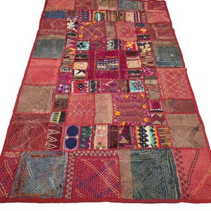 May include: A rectangular patchwork rug featuring a vibrant array of stitched fabric squares in shades of red, pink, blue, and yellow. The textile displays intricate embroidery, geometric patterns, and small decorative pom-poms throughout the surface.