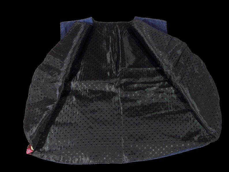 May include: A blue denim vest with a black lining featuring a small polka dot pattern. The vest is unbuttoned and turned inside out, showing the lining.