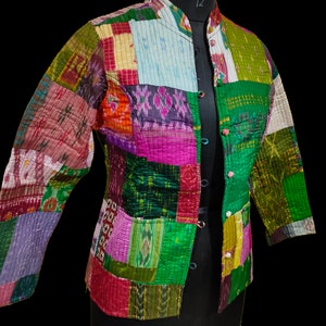 Puede incluir: Una chaqueta de patchwork con cuello mandar&iacute;n y cierre de botones. La chaqueta est&aacute; hecha de una variedad de telas coloridas, incluyendo verde, rosa, morado y azul.