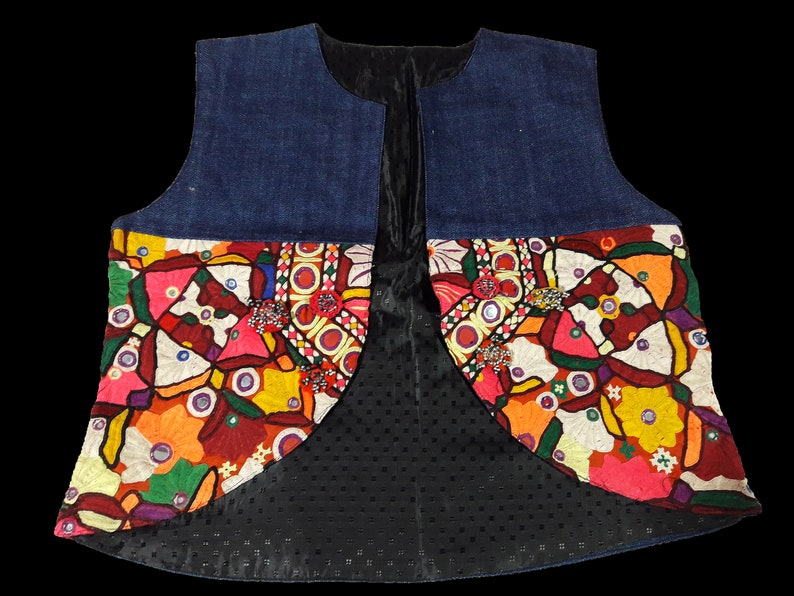 May include: A denim vest with colorful embroidered patches and mirror accents. The vest has a black lining with a dotted pattern.